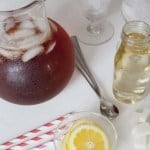 Pitcher of iced tea, bottle of simple syrup, lemon slices, and straws.