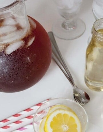 Pitcher of iced tea, bottle of simple syrup, lemon slices, and straws.