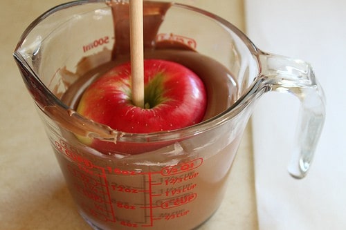 Dipping red apple in melted milk chocolate.
