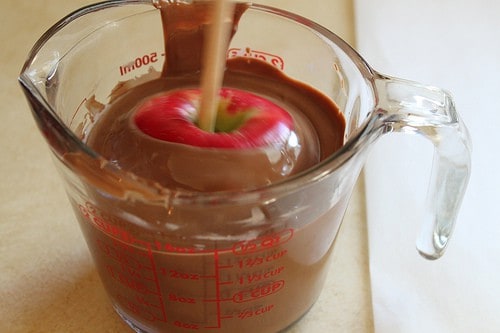 Dipping apple in measuring cup filled with melted milk chocolate.