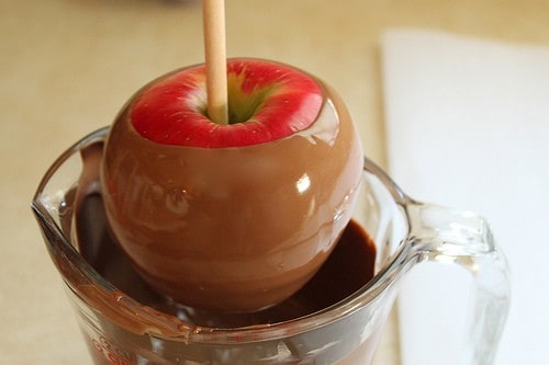 Dipping a red apple in milk chocolate.