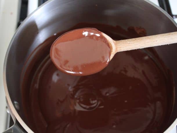 Melted chocolate on wooden spoon over a pan.