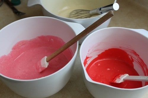 Pink and red cupcake batter in white bowls.