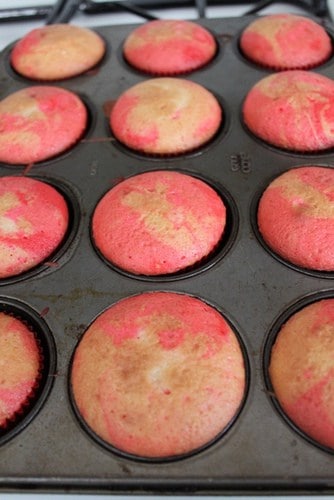 Baked pink and white tie dyed cupcakes in a muffin pan.