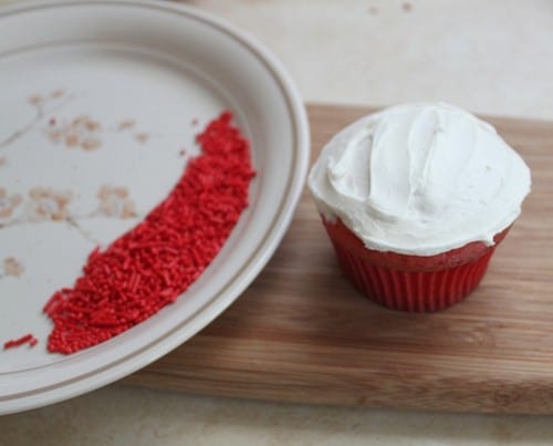 White frosted cupcake. Red sprinkles on dinner plate.