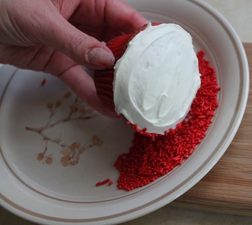 Rolling edge of white frosted cupcake in red sprinkles.