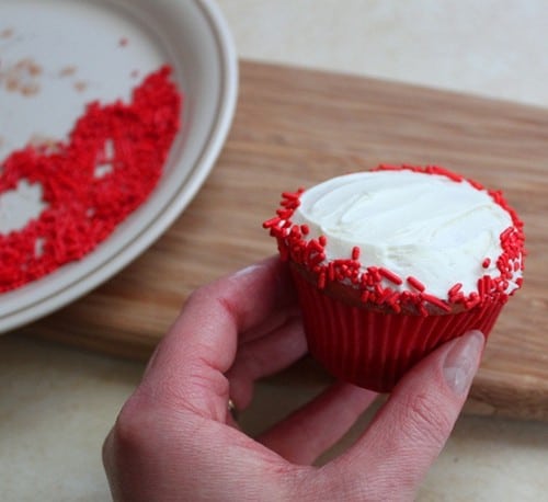White frosted cupcake with red sprinkles on the edge.