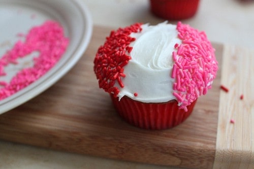 White frosted cupcake with red and pink sprinkles.