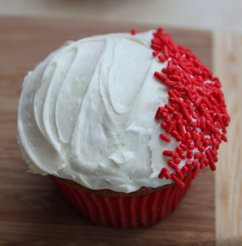 White frosted cupcake with red sprinkles on the right side.
