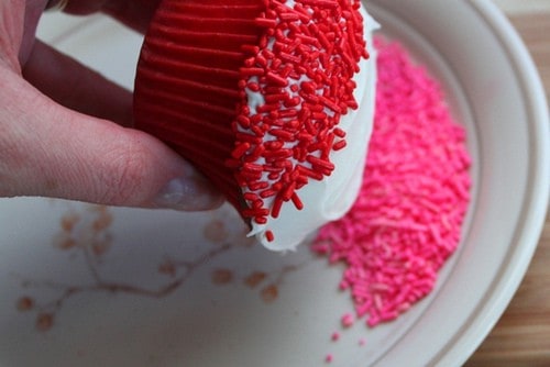 Dipping top of frosted cupcake in pink sprinkles.