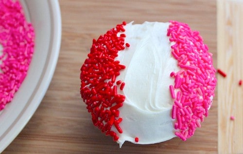 Gluten-free cupcake with white frosting and red and pink sprinkle stripes.