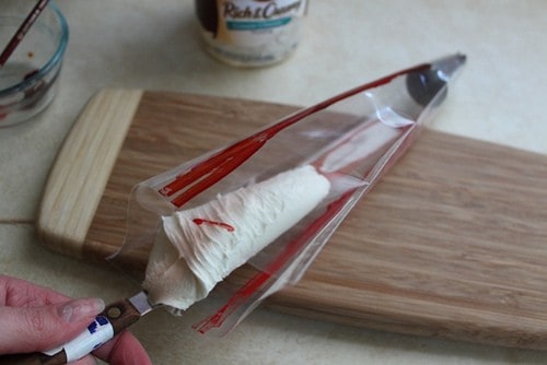 Filling pastry bag with white frosting. Bag is striped with red food color.