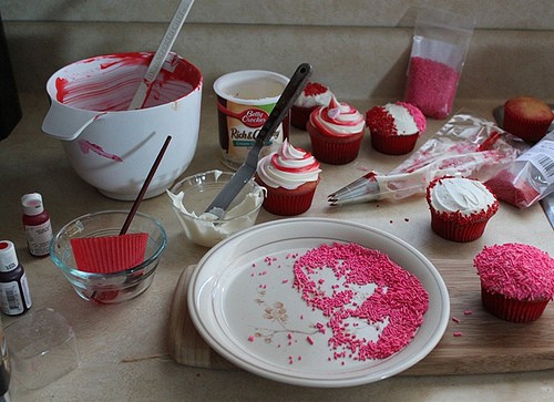 Messy kitchen counter with frosting, sprinkles, and cupcakes.
