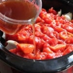 Pouring broth into slow cooker filled with crushed tomatoes.