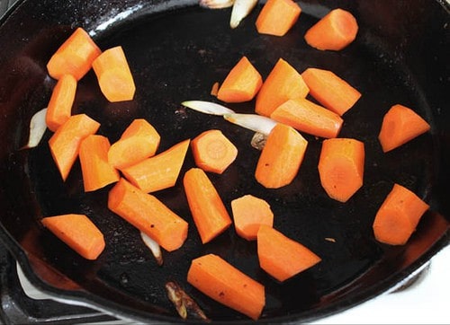 Carrots cooking in black skillet for paleo pot roast.