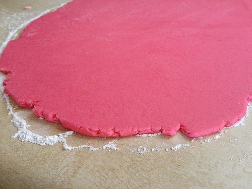 Pink gluten-free sugar cookie dough rolled out on a counter.