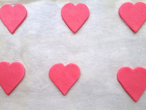 Pink gluten-free sugar cookie dough hearts on a baking pan.
