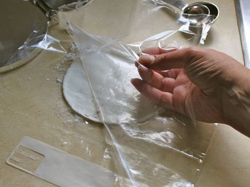 Gluten-Free Flour Tortilla dough pressed between a piece of plastic.