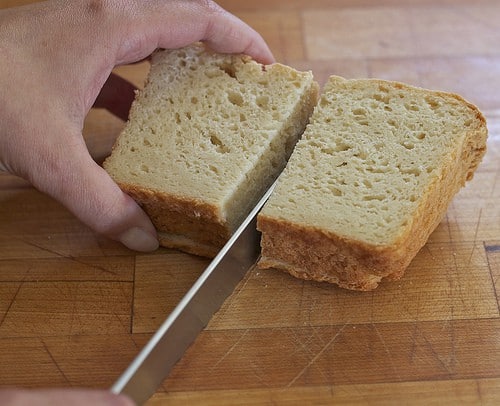 Cutting three slices of gluten-free bread in half for bread crumbs.