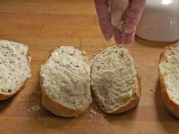 Sprinkling cheese and herbs on gluten-free bread for garlic bread.