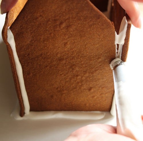 Placing icing on sides of gluten-free gingerbread house.