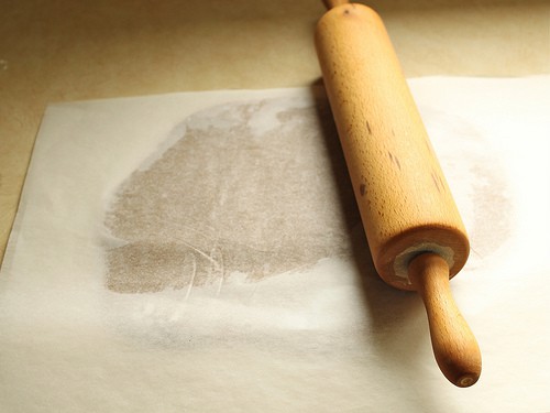 Gluten-free gingerbread dough between two pieces of parchment paper.