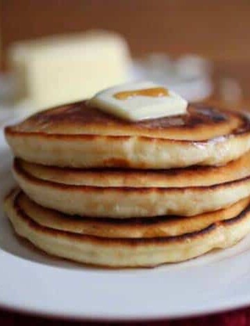 Stack of gluten-free pancakes with pat of butter and drizzle of syrup.
