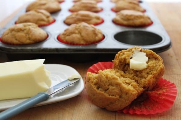 Gluten-Free Pumpkin Muffin split and spread with butter. Pan of muffins and stick of butter in background.