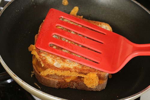 Pressing down a gluten-free grilled cheese with spatula in pan.