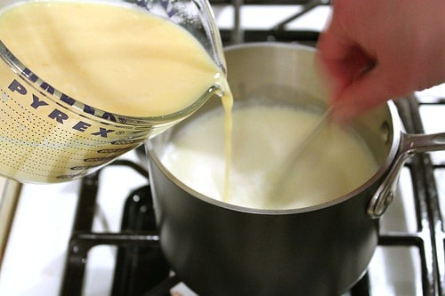 Pouring tempered egg mixture into pot of milk for homemade eggnog.