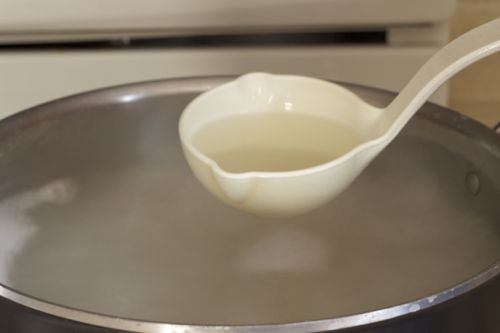 A white ladle removes a cup of pasta water from pot.