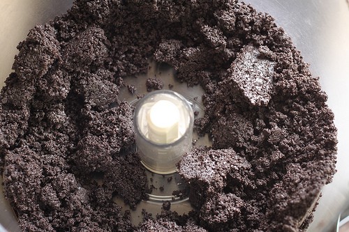 Gluten-free chocolate sandwich cookie crumbs in bowl of food processor.