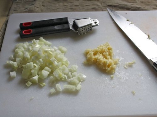 Chopped onion and minced garlic on a cutting board.