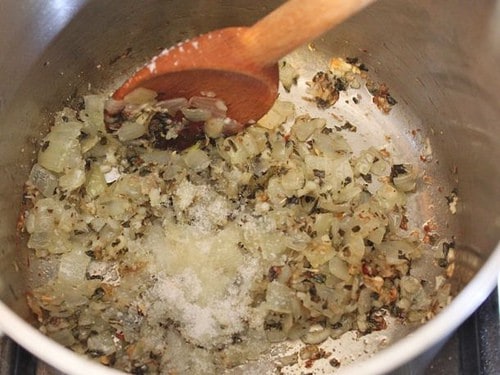 Cooked onions, garlic, and herbs in a pot. Salt and sugar added.