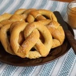Gluten-free pretzels on a plate with a jar of mustard sitting to the right.
