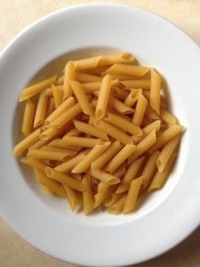 Uncooked gluten-free pasta in white bowl.