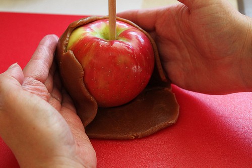 Wrapping a red apple in caramel.