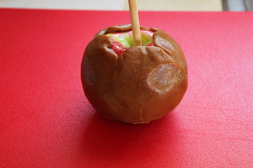 Caramel coated apple on red cutting board.