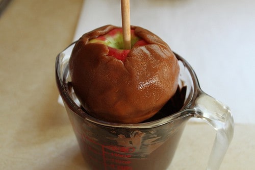 Caramel coated apple being dipped in chocolate.
