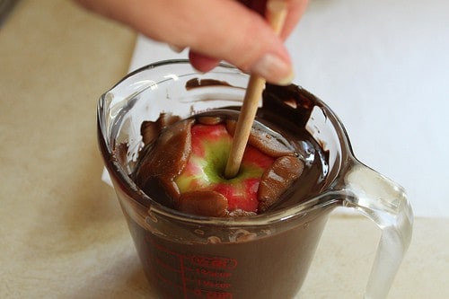 Dipping caramel coated apple in dark chocolate.