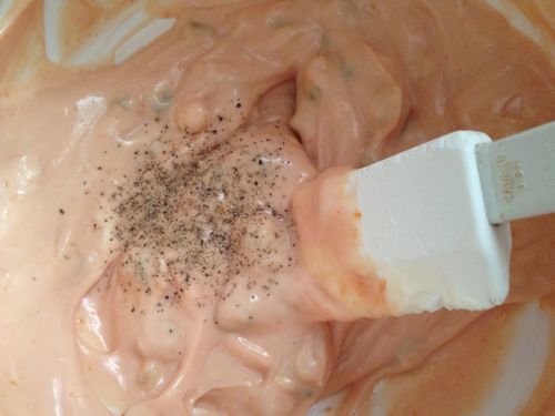 Stirring black pepper into special burger sauce with rubber spatula.