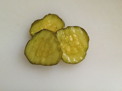 Three pickle slices on a cutting board.