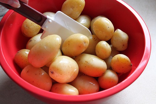 Stirring steamed potatoes and melted butter with a rubber spatula.