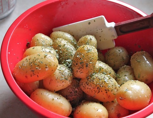 Steamed potatoes in a red bowl with butter and herbs.