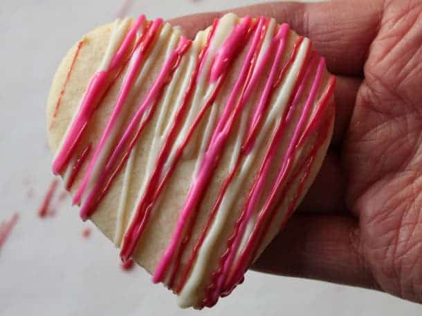 Gluten-free sugar cookie hearts frosted with red, pink, and white drizzle.