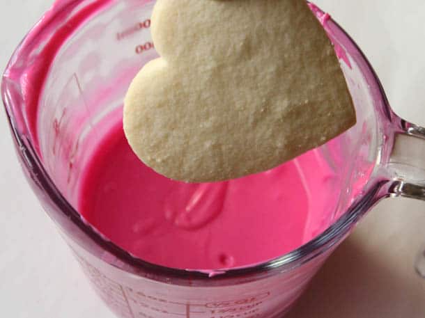 Heart shaped gluten-free sugar cookie about to be dipped in pink chocolate.