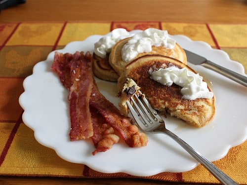 Gluten-free chocolate chip pancakes topped with whipped cream on a plate with bacon.