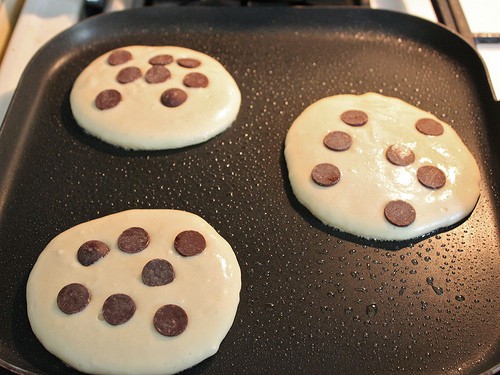 Chocolate chips on top of gluten-free pancakes cooking on a griddle.