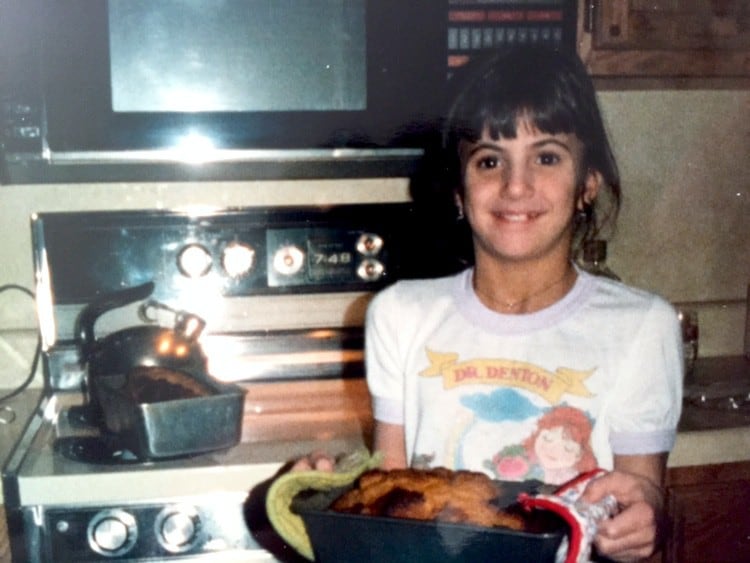 Elizabeth Barbone Childhood Photo. Standing in front of an oven, holding a pan of bread.