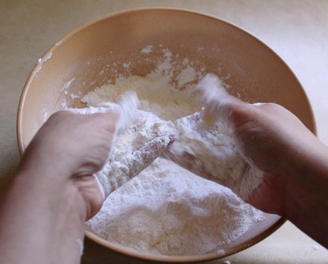 Two hands mix butter into gluten-free cobbler mixture.